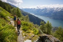 To personer på tursti med utsikt over fjord og fjell.