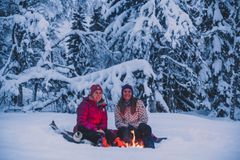 To personer ved et bål i en snødekt skog.