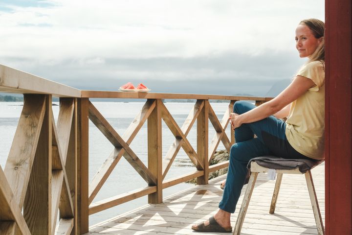 Kvinne sitter på en terrasse med utsikt over en fjord.