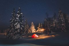 Et rødt telt i en snødekt skog om natten, omgitt av stjerner på himmelen.