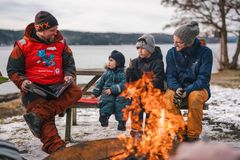 En gruppe mennesker sitter ved et bål ved vannet om vinteren.