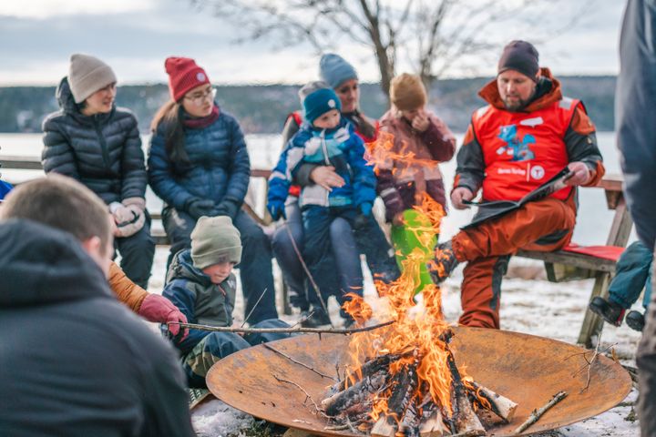 En gruppe mennesker sitter rundt et bål ute i vinterlandskap.