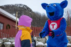 En person i fargerik turjakke møter en stor, blå maskot med store ører utendørs i et snødekt landskap.