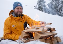 Person i gul jakke tenner et bål i snøen.