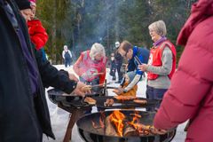 Folk griller pølser på bål i en snødekt skog.