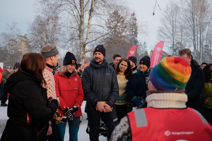 En gruppe mennesker kledd i vinterklær står sammen utendørs. Noen av dem smiler. Det er snø på bakken, og noen trær i bakgrunnen.