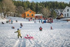 Barn leker i snøen foran trehus, omgitt av skog.