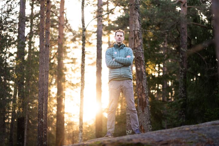 En mann står i en skog med solnedgang i bakgrunnen.