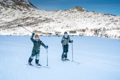 To personer står på ski i et snødekt landskap med fjell i bakgrunnen.