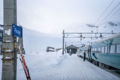 Tog stopper på snødekt perrong ved Finse stasjon med ski lent mot en stolpe.