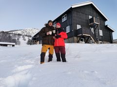 To personer står foran en snødekket bygning i vinterklær, Solheimstulen.