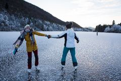 To personer står på skøyter på en frossen innsjø omgitt av snødekte trær.