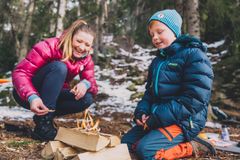 En kvinne og et barn forbereder bål i skogen. De er kledd i varme jakker.