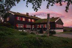 Alternativ tekst: Nedalshytta med torvtak ved solnedgang, omgitt av grønt landskap.
