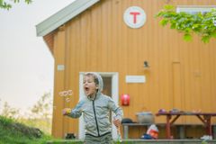 En gutt blåser såpebobler foran en gul DNT-hytte
