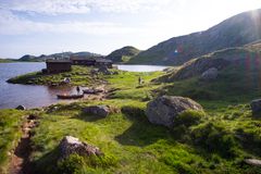 Et idyllisk landskap ved Øyuvsbu i Setesdalen med hytte ved vannet, grønn vegetasjon og omkransende fjell.