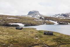 En hytte ved en innsjø i et fjellandskap med spredt snø.