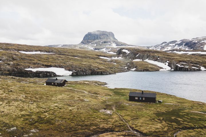 En hytte ved en innsjø i et fjellandskap med spredt snø.