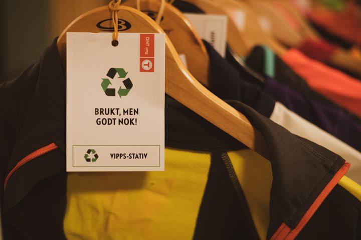 En henger med brukte klær har en etikett med teksten: "Brukt, men godt nok!" og et resirkuleringssymbol.