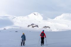 To personer på ski beveger seg mot en fjellhytte i et snødekket landskap.