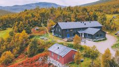 To store trebygninger omgitt av høstfargerike trær ved foten av et fjell.