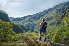 En person med ryggsekk står på en stein og ser utover en frodig dal med høye fjell i Aurlandsdalen.