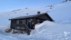Den lille brune hytta, Stordalsbu, står omgitt av snødekte fjell og lave snøbanker.