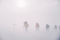 Vandrere med ryggsekker går i tykk tåke på fjellet.
