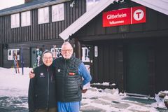Et smilende par står foran DNT-hytta Glitterheim i et snødekket landskap.
