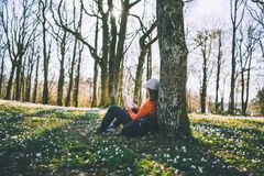 person som sitter lent inn på et tre og leser bok. Rundt personen er det masse hvitveis