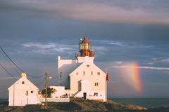 bilde av et hvitt fyr som står på et berg. i bakgrunnen ser man en regnbue og havet.