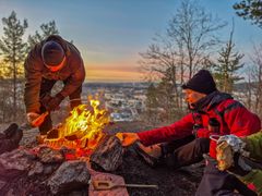 personer som sitter rundt et bål. i bakgrunnen ser man en by