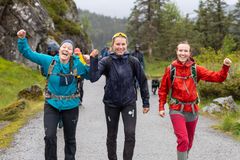 Tre glade personer går på en sti i et skogsområde, iført turklær.