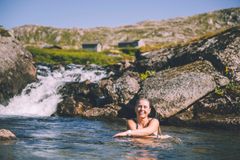 Kvinne som bader i et vann. Fjellandskap i bakgrunnen.