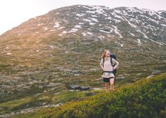 Kvinne skuer utover fjellandskap. Det er sol.
