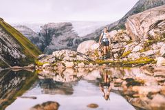 En person går på tur i fjellet, omgitt av steiner og en rolig vannoverflate som speiler landskapet.