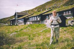 Kvinne som står i fjellandskap smiler til kamera. Bak henne ligger ei brun hytte.