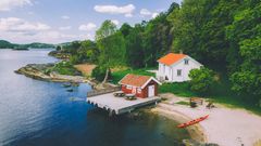 Et båthus og en hytte ved en rolig kystlinje med en liten brygge og kajakk.
