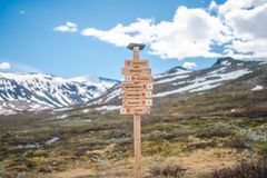 Skilt på fjellsti med retninger til forskjellige turmål, fjellandskap i bakgrunnen.