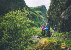 To personer går på en tursti i en grønn og frodig dal med bratte fjellsider i Aurlandsdalen.