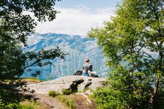 En person sitter på et utsiktspunkt på Dronningstien, omgitt av trær, med fjell i bakgrunnen.