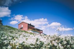 Et rødt turisthyttebygning på en grønn åsside under en blå himmel med noen skyer.