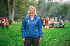 En kvinne står ute på en gressplen med mennesker i bakgrunnen. Hun har på seg en blå jakke med DNT-logoen.