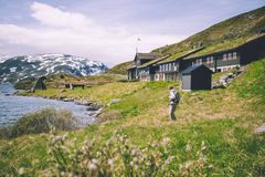 Person med ryggsekk går på gresskledd område nær Haukeliseter, omgitt av fjell og vann.