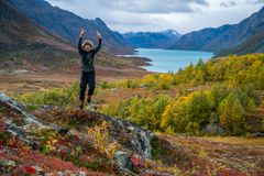 En person hopper av glede i et fargerikt høstlandskap med fjell og en innsjø i bakgrunnen.