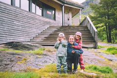 En kvinne sitter på huk sammen med to barn utenfor hytta Jonstølen i Ryfylke, med trapp og fjellside i bakgrunnen.