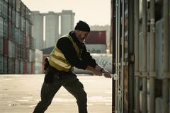 Toller står langs mange containere. Han bruker et brekk for å åpne plomben på en container.