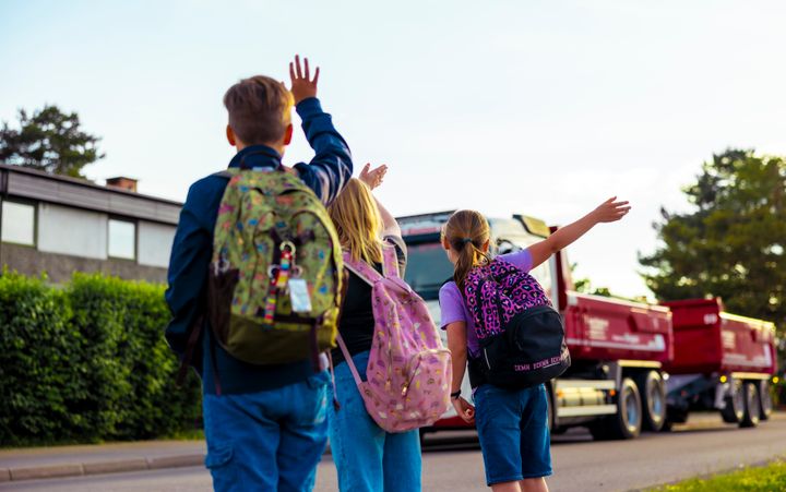 Skolebarn vinker til en lastebil som kjører forbi