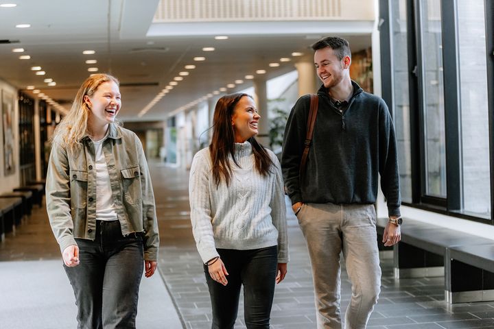 Tre glade studenter som går i en opplyst korridor.