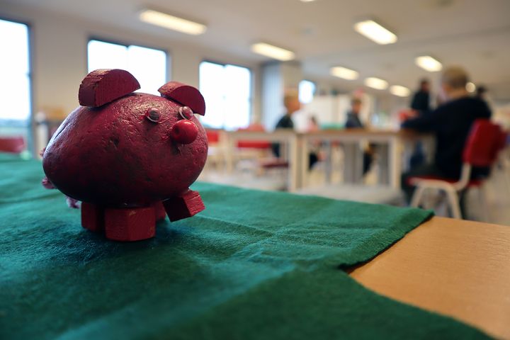 Rødmalt gris av stein på et bord i et klasserom med klasseromsaktivitet i bakgrunnen.
